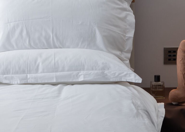 Suction cup dildo placed on nightstand next to white bed