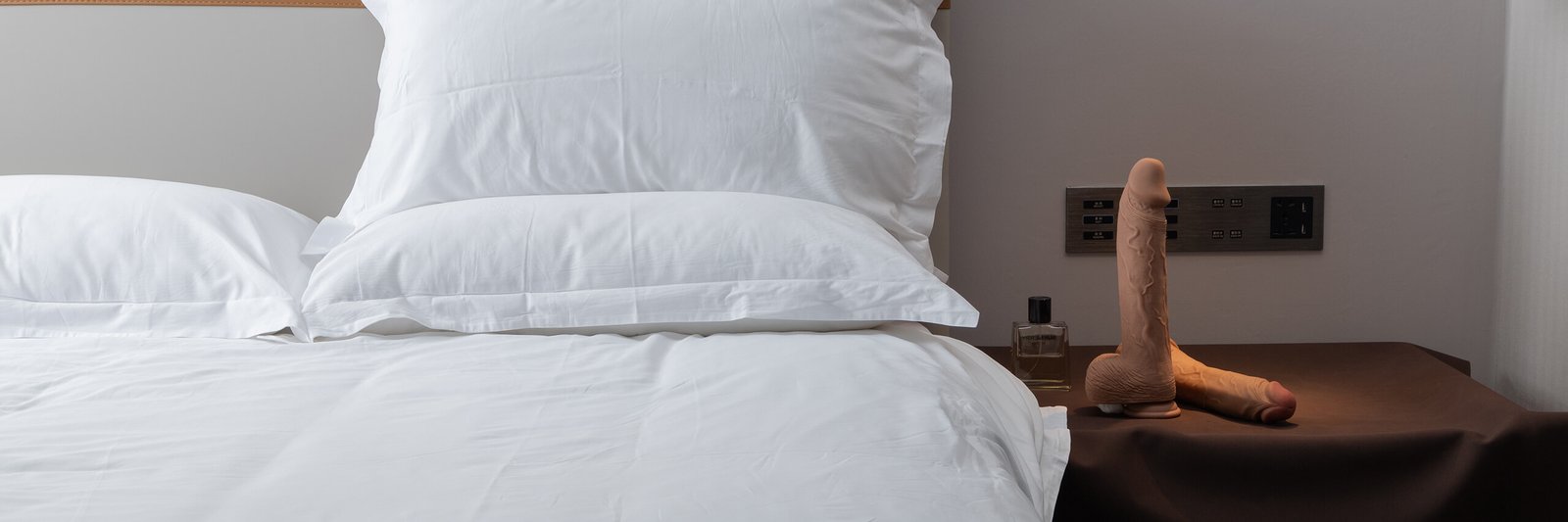 Suction cup dildo placed on nightstand next to white bed