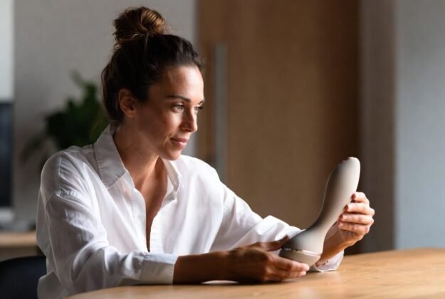 Sexual wellness professional examining a minimalist body-safe product prototype, representing the bridge from therapist insights to manufacturable sexual wellness products